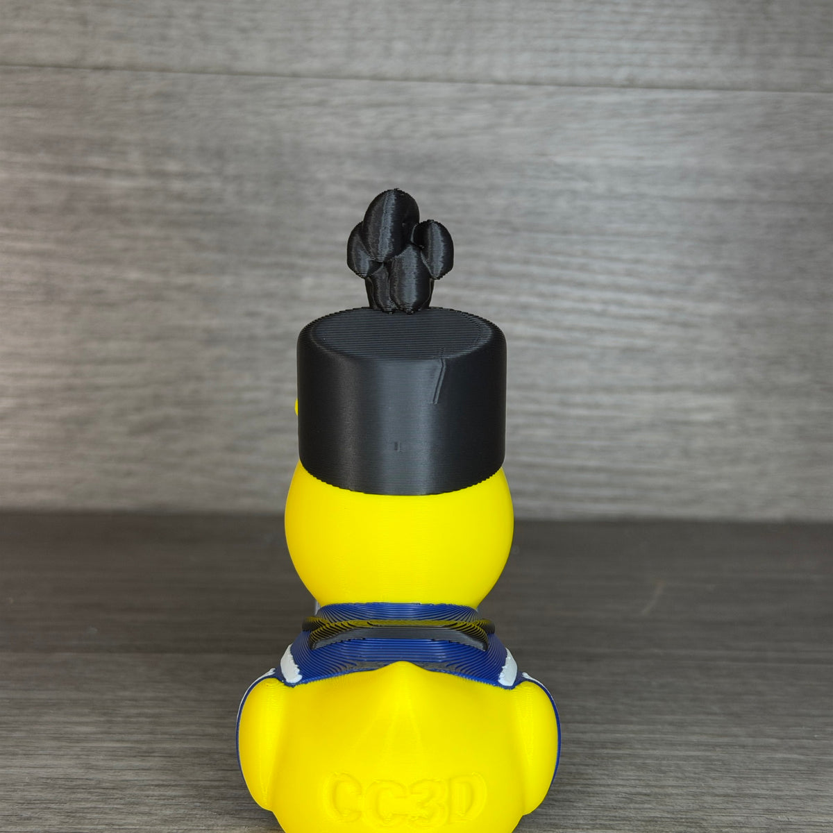 Straight-on back view of the drummer duck with black plumed hat, blue collar and CC3D engraved on the tail