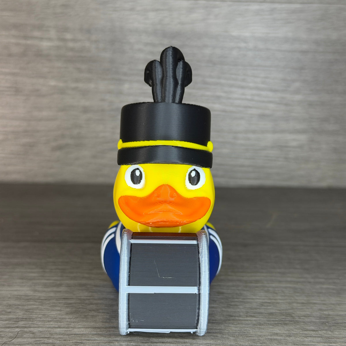 Front view of the band drummer duck showing its face, orange bill, black band hat with yellow chin strap and the bass drum in front