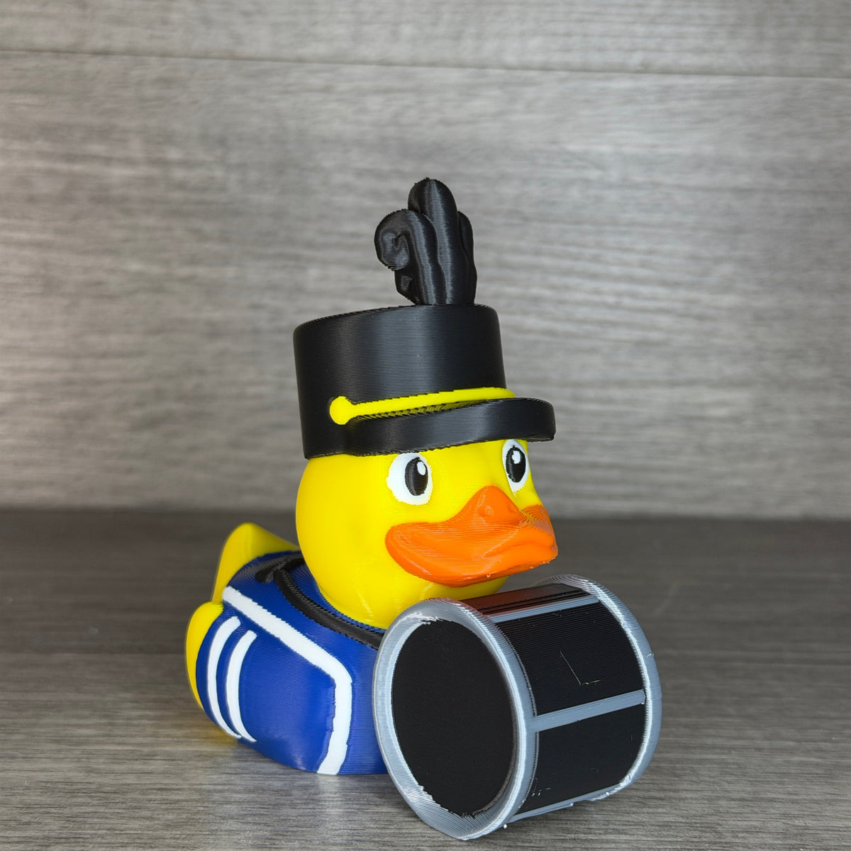 Angled view of the drummer duck in a blue and white band uniform with a black drum harness and silver-rimmed bass drum