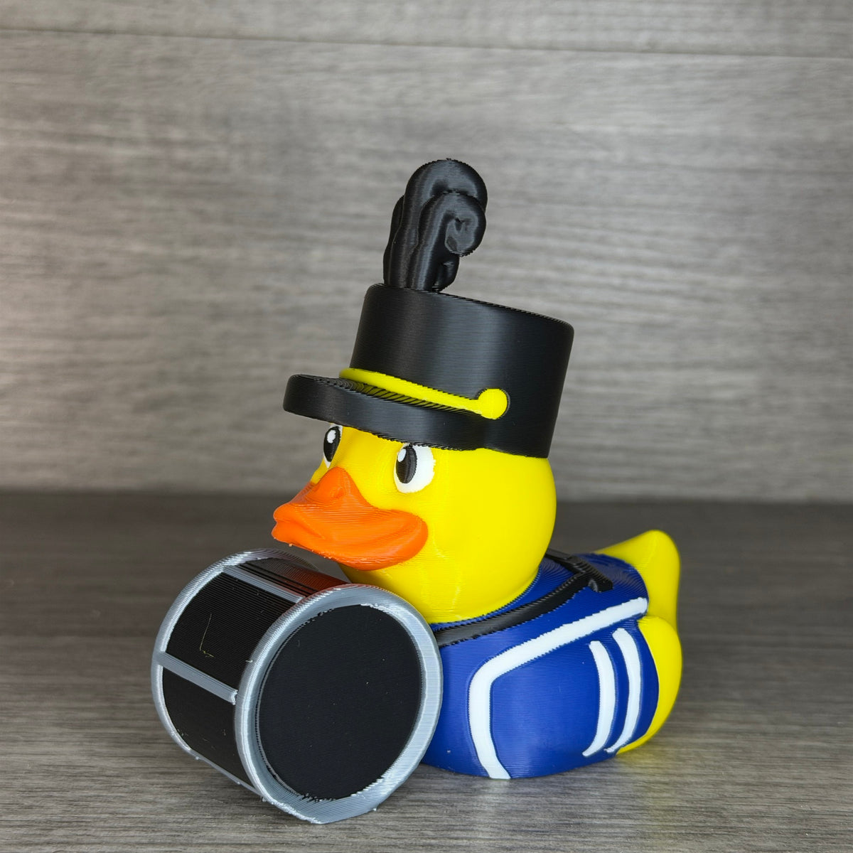 Left side angle of the marching band duck showing the plume, hat brim with yellow strap and the round black drum head