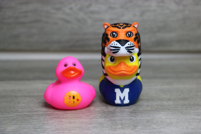 Two rubber duck toys, one pink and one with a tiger design, on a gray surface.