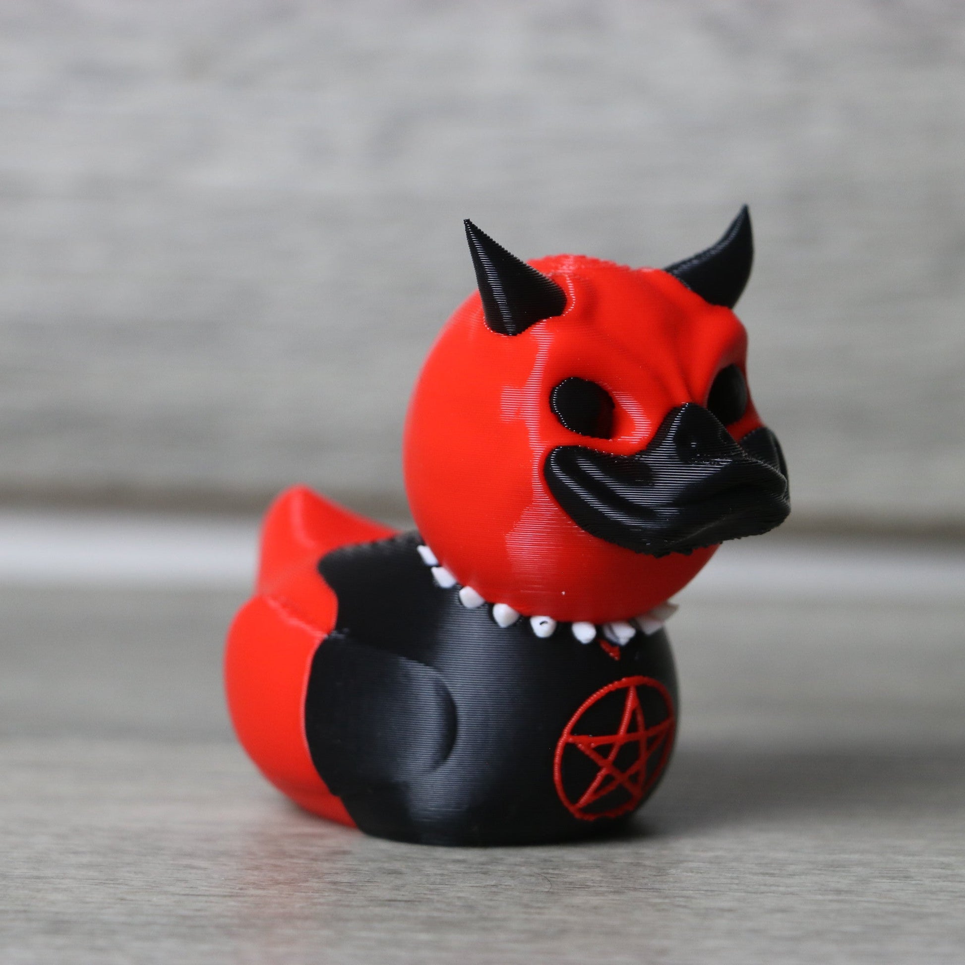 Red and black figurine with horns and a pentagram symbol on a gray background
