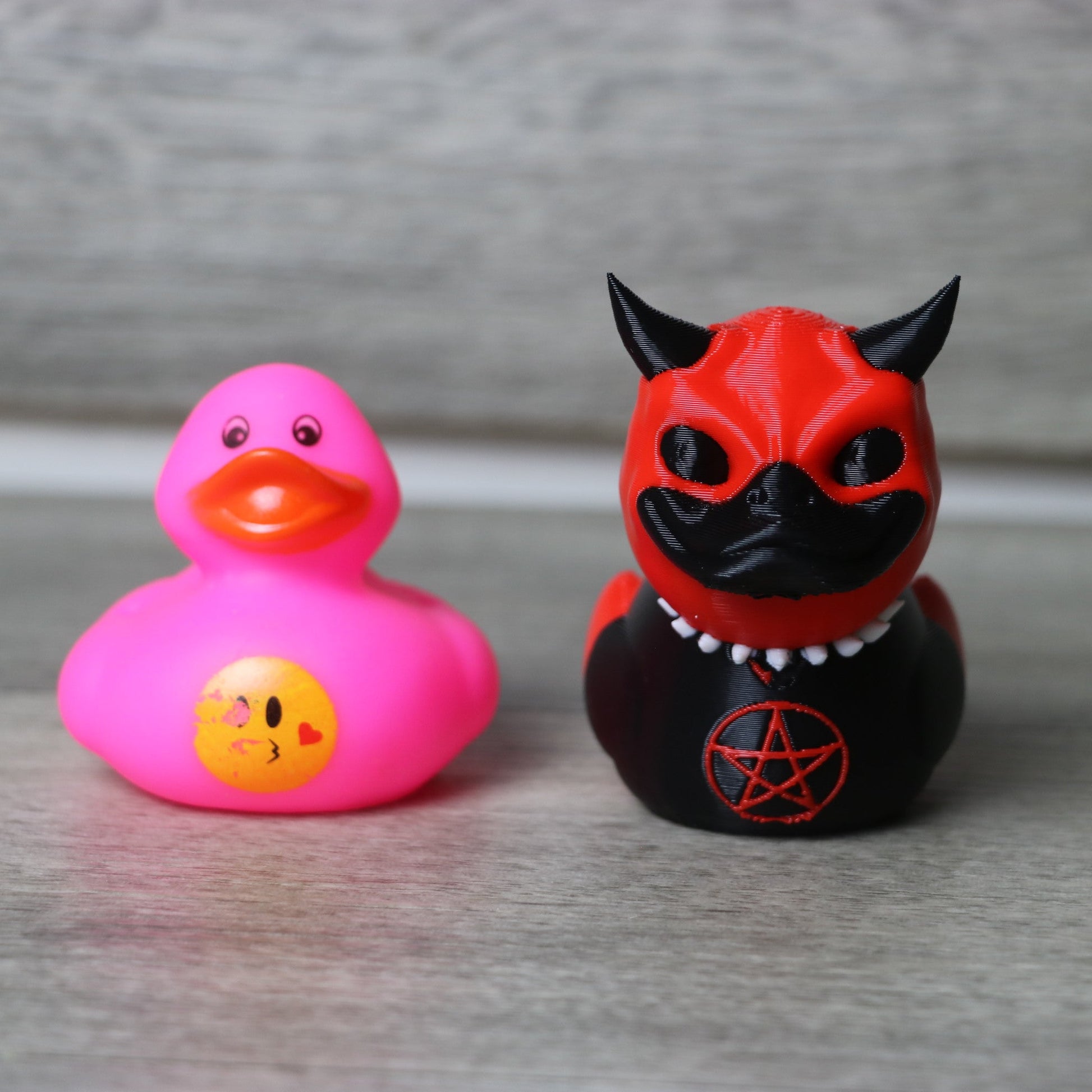 Pink rubber duck and black and red devil-themed figurine on a gray surface