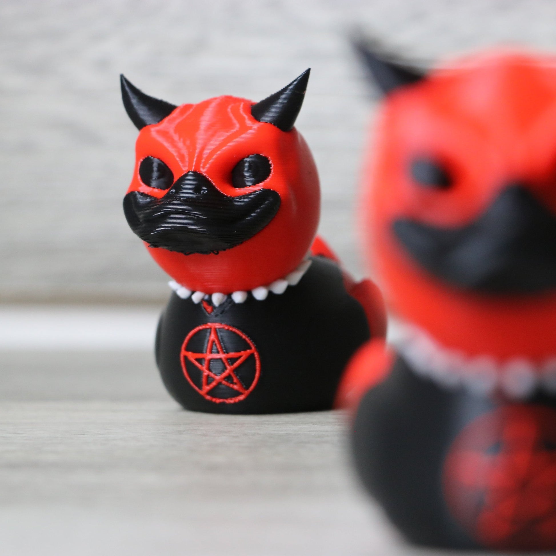Two red and black figurines with a pentagram symbol on a neutral background