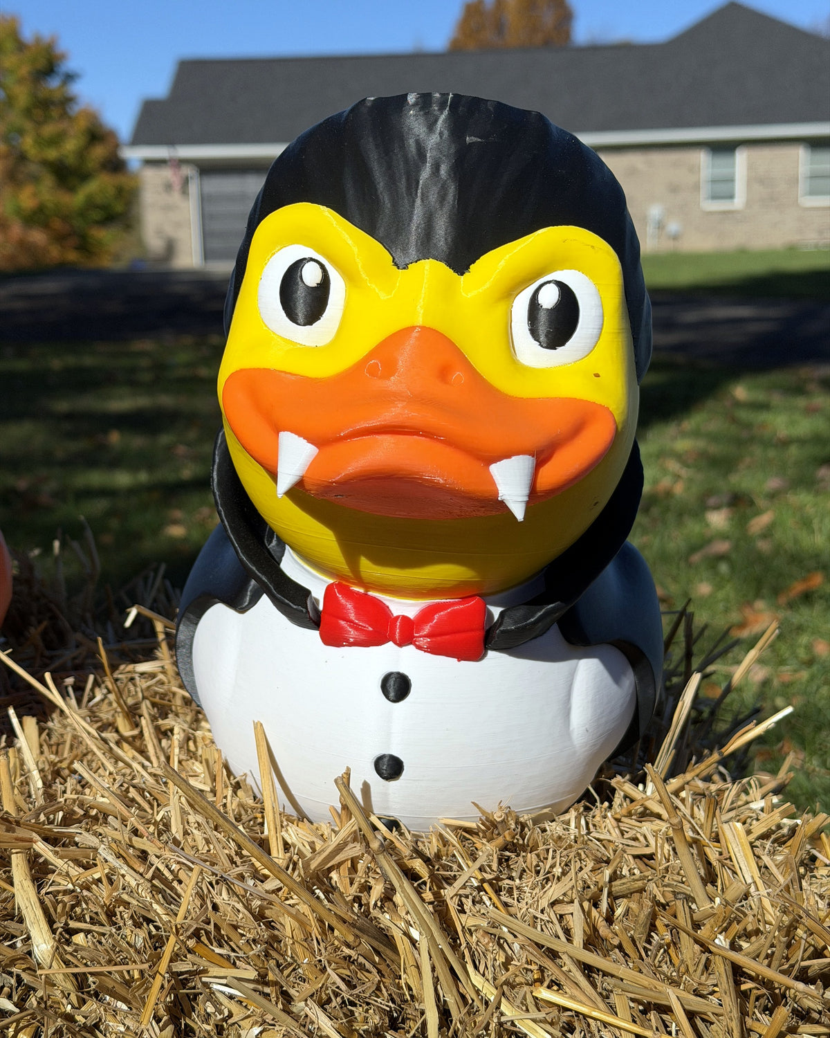 Giant Vampire Duck 12 inch 3D printed Dracula duck with fangs and bow tie, outdoors on a hay bale