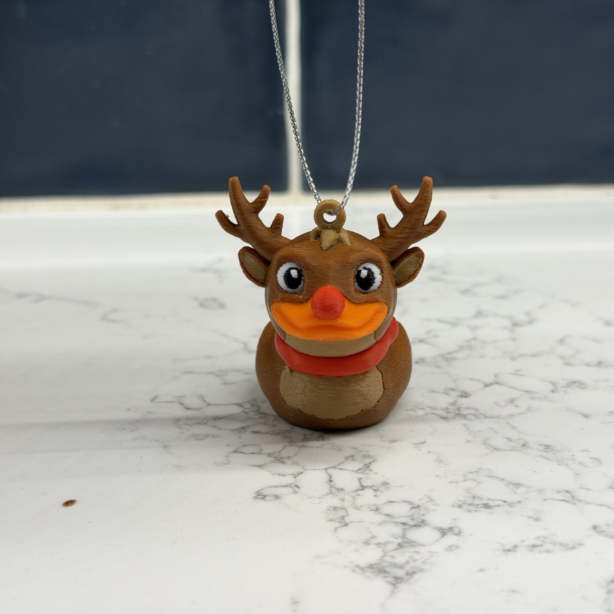Front view of the reindeer duck ornament on a marble counter with its silver hanging string