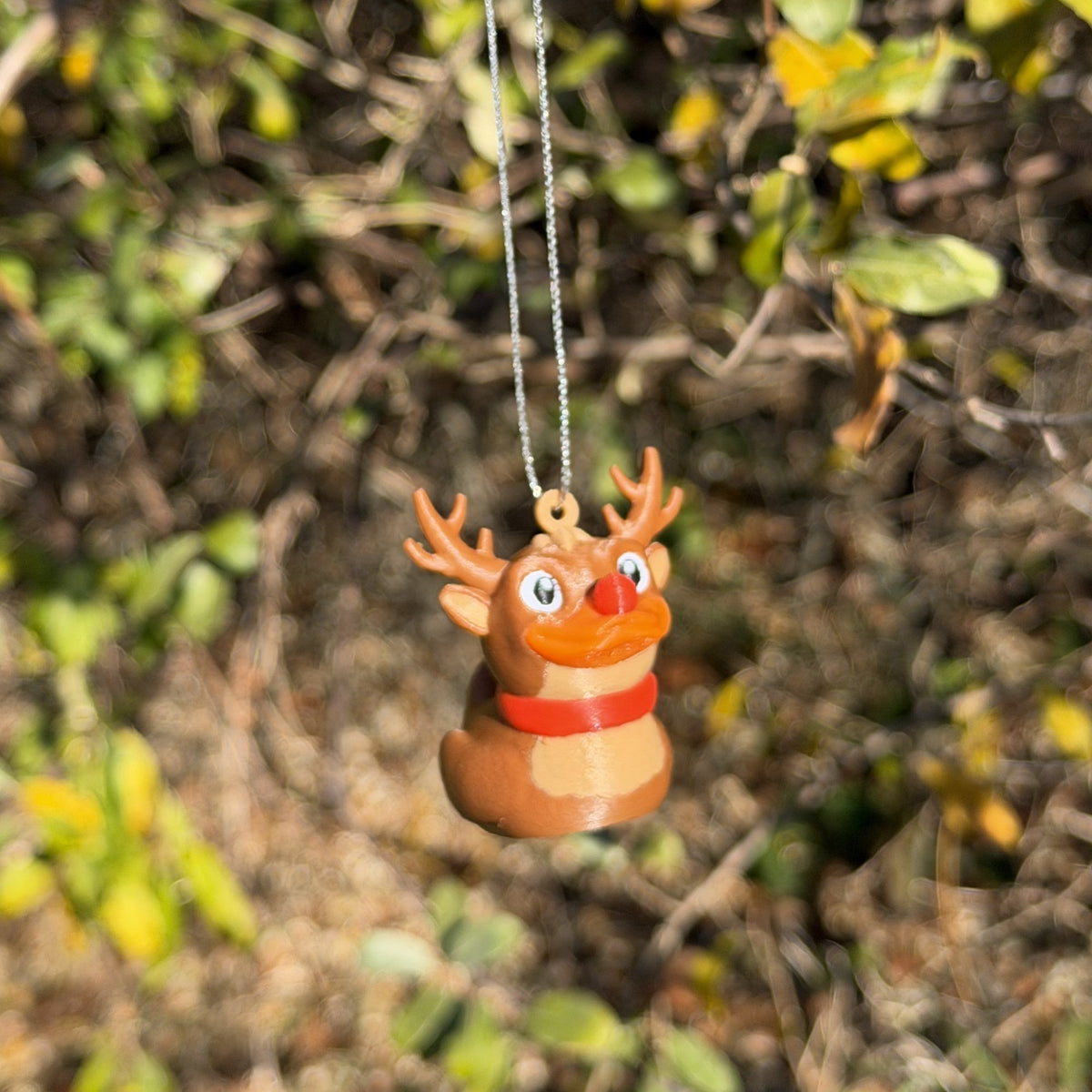 Small reindeer duck ornament hanging on a silver string in front of autumn leaves