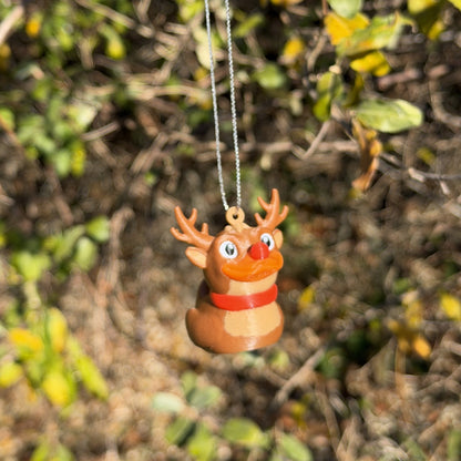 Small reindeer duck ornament hanging on a silver string in front of autumn leaves