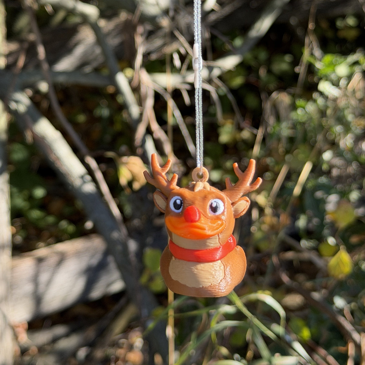 Reindeer duck ornament hanging from a branch, showing its antlers, red nose and red scarf